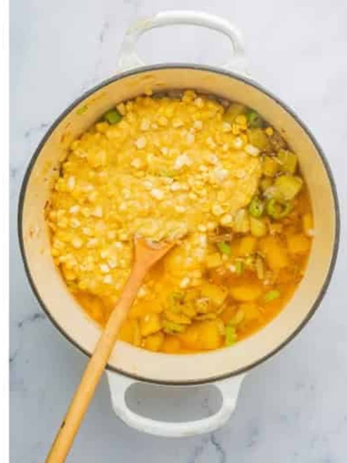 Adding cream style corn and broth to the pot of vegetables for corn chowder.