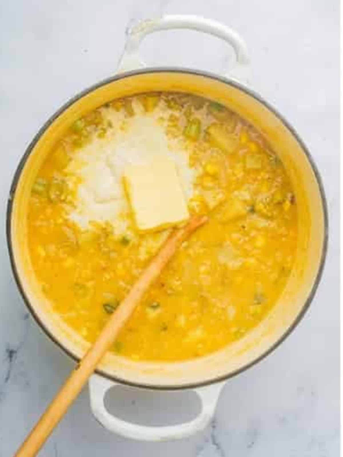 Adding butter to the simmering pot of corn chowder.