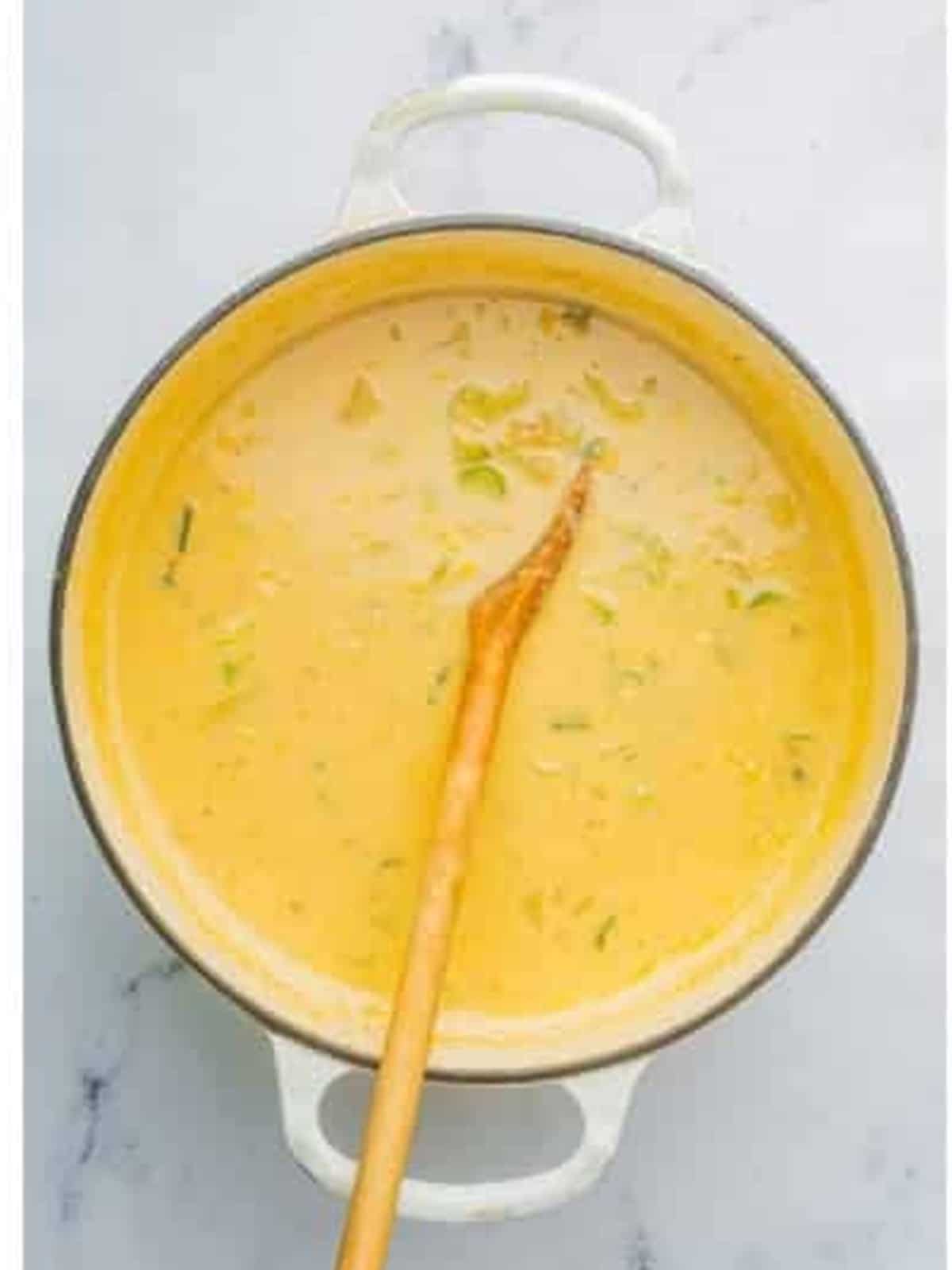 Stirring heavy cream into the creamy corn chowder in a white pot.