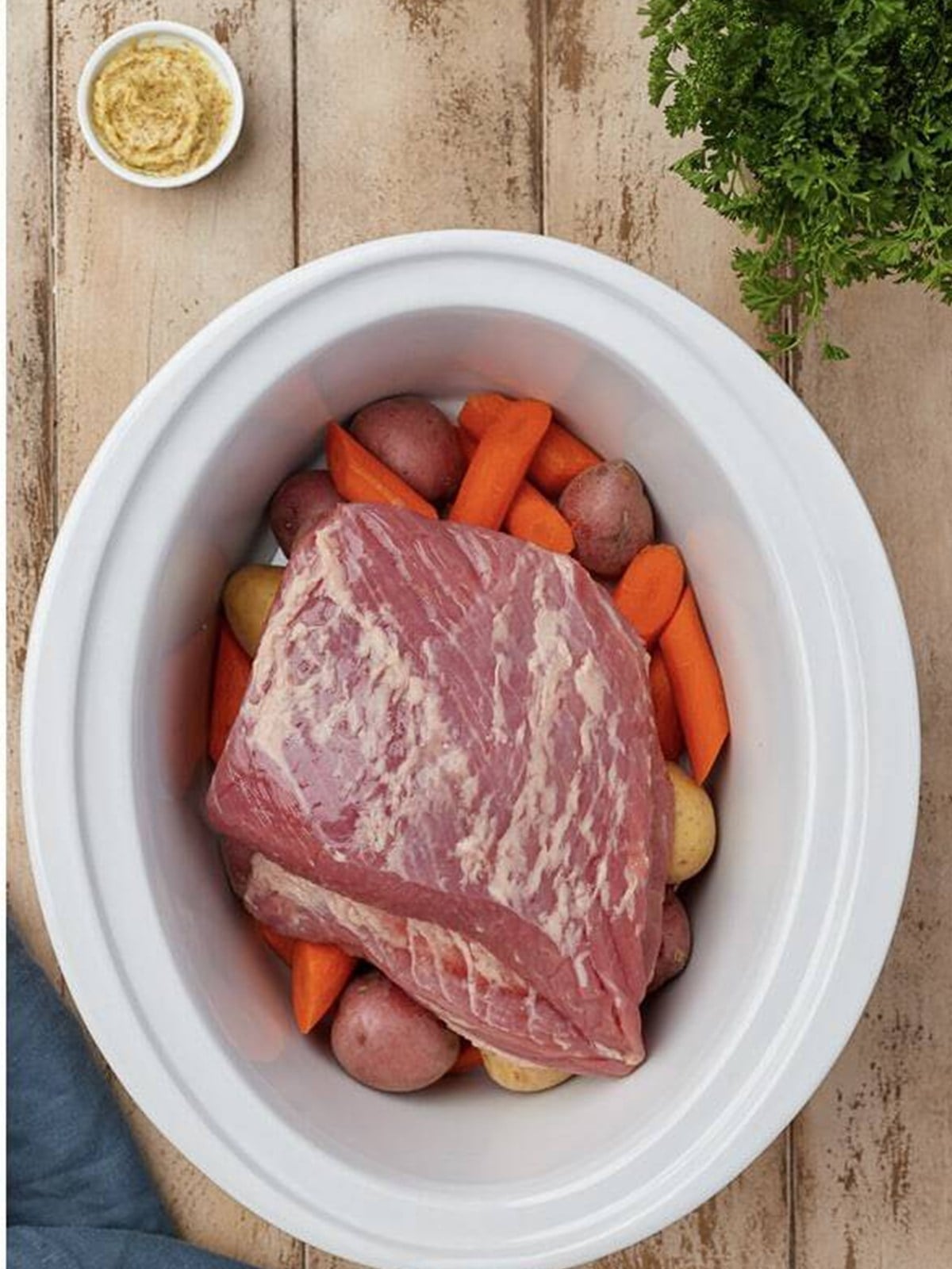 Corned beef brisket placed on top of the potatoes and carrots in the slow cooker.