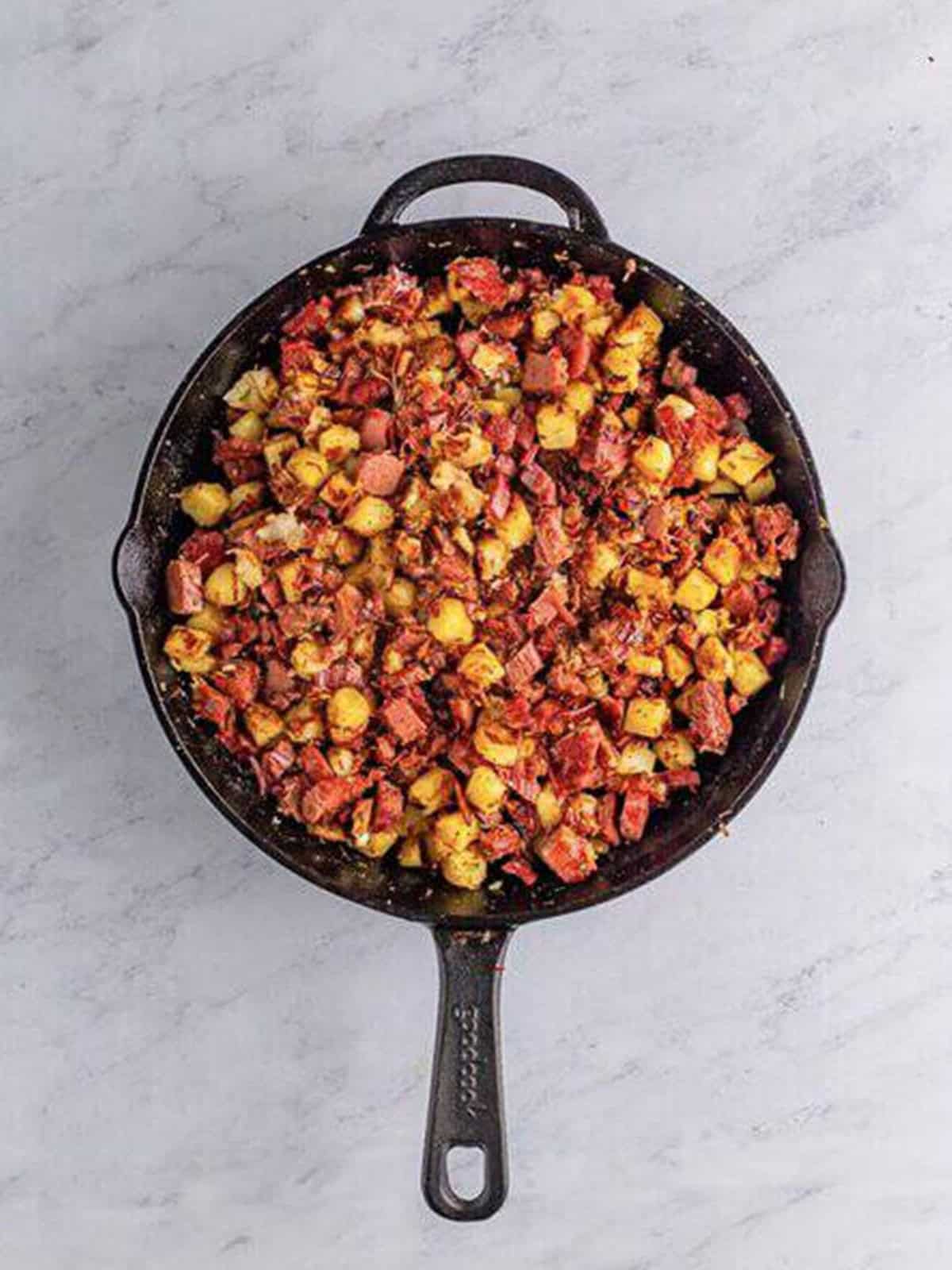Corned beef hash browning in a cast iron skillet until crispy.