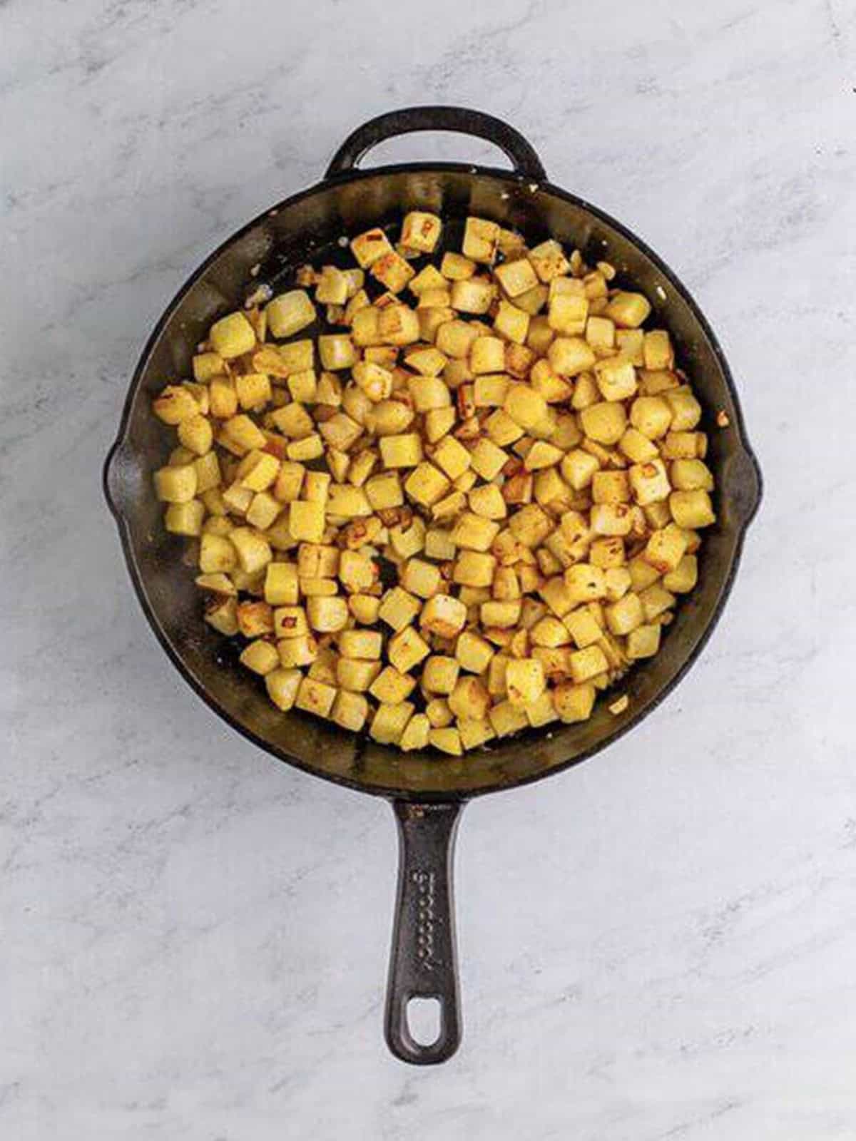 Diced potatoes and onion cooking in butter in a cast iron skillet for corned beef hash.