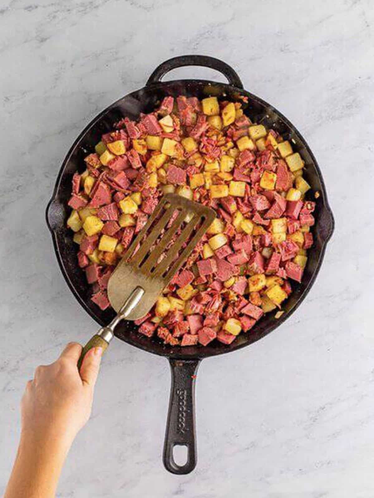 Corned beef hash pressed into an even layer to form a crispy crust in a skillet.
