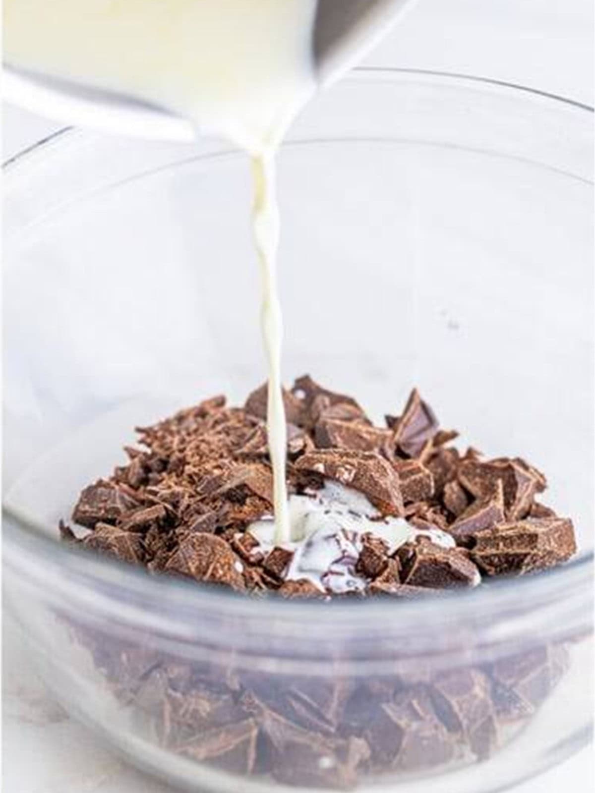 Pouring hot heavy cream over chopped chocolate to make ganache.
