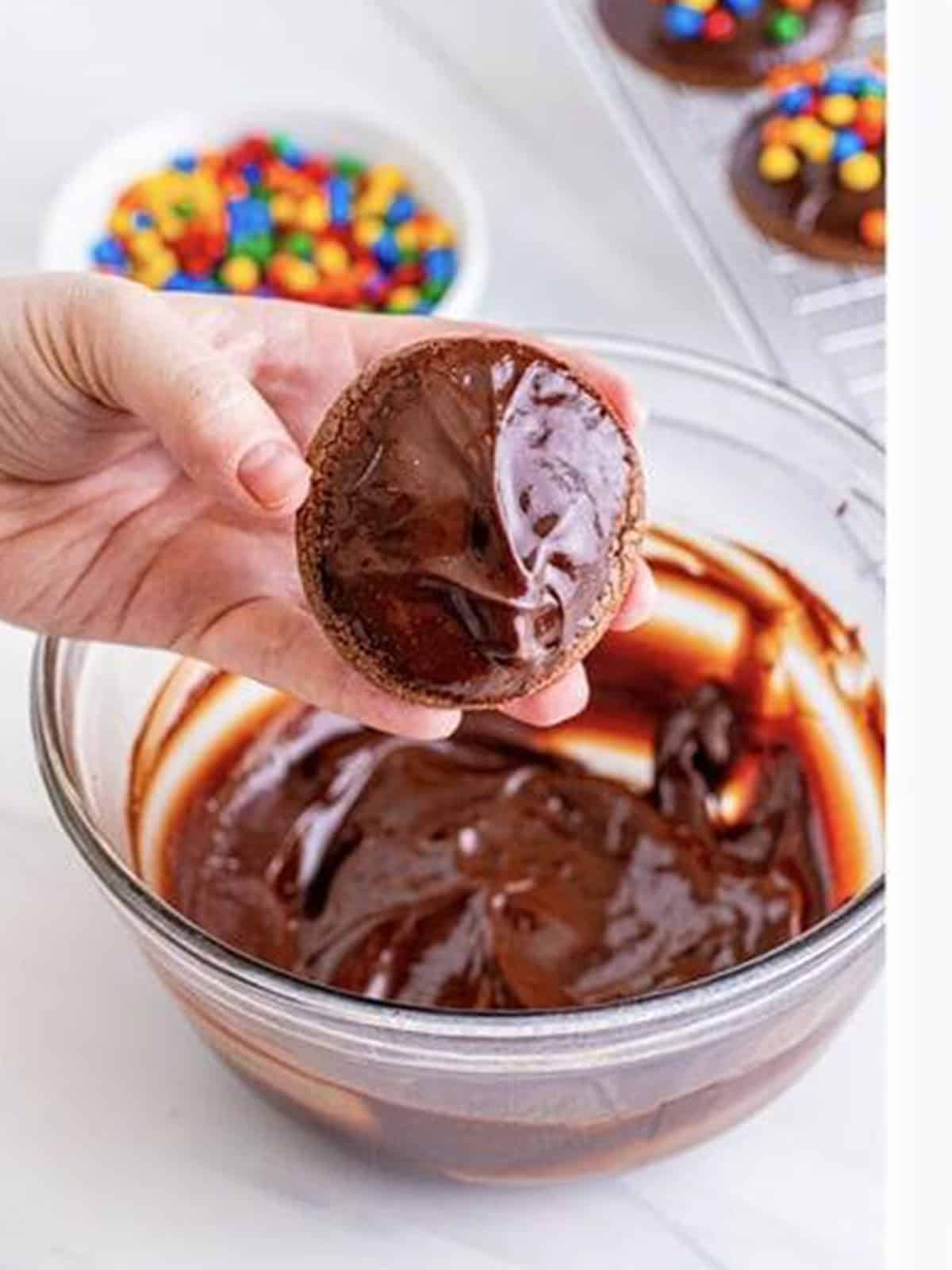 Dipping a cooled brownie cookie into smooth chocolate ganache.