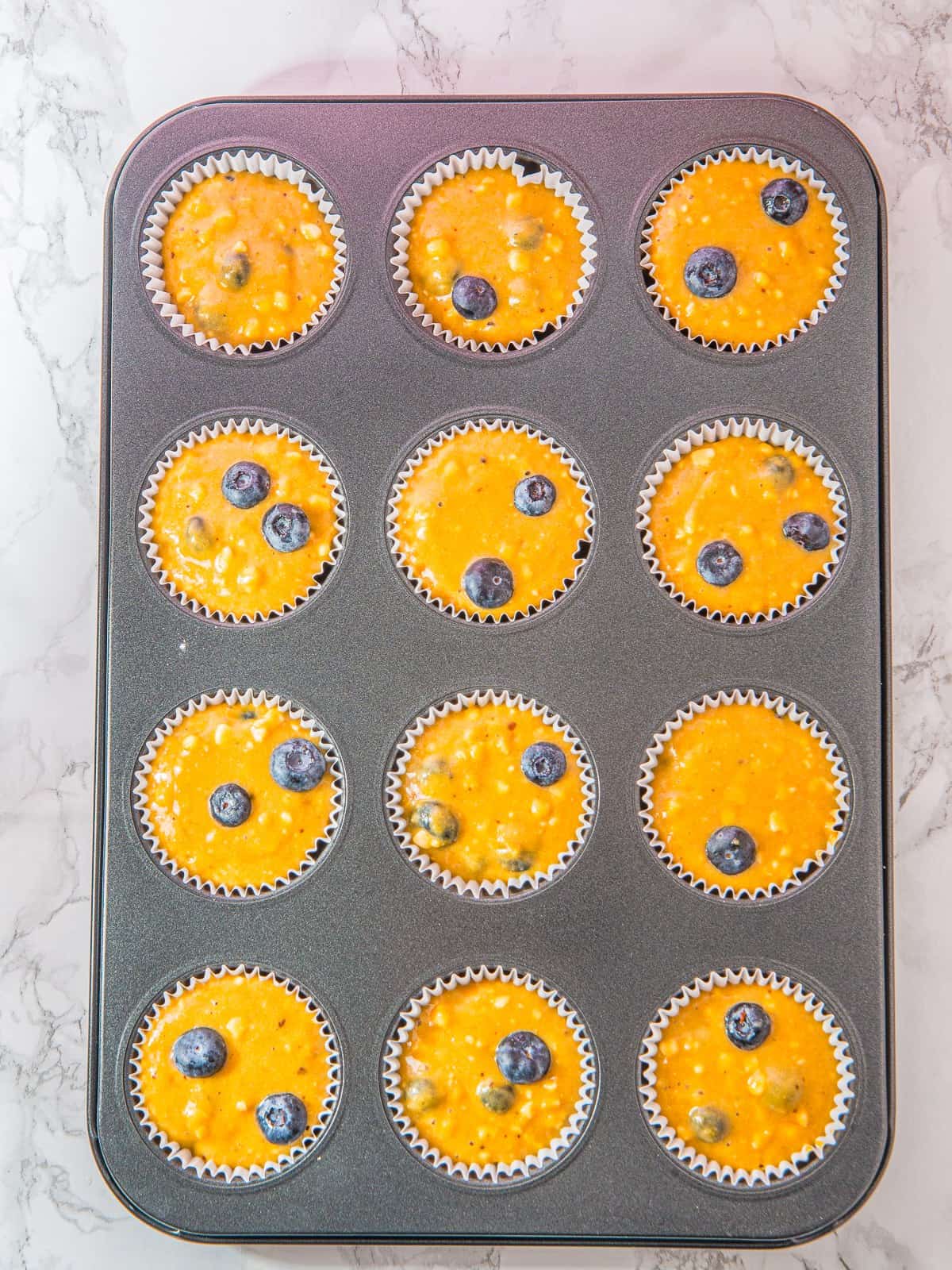 Muffin batter portioned into a lined muffin tin for Cottage Cheese Blueberry Muffins.