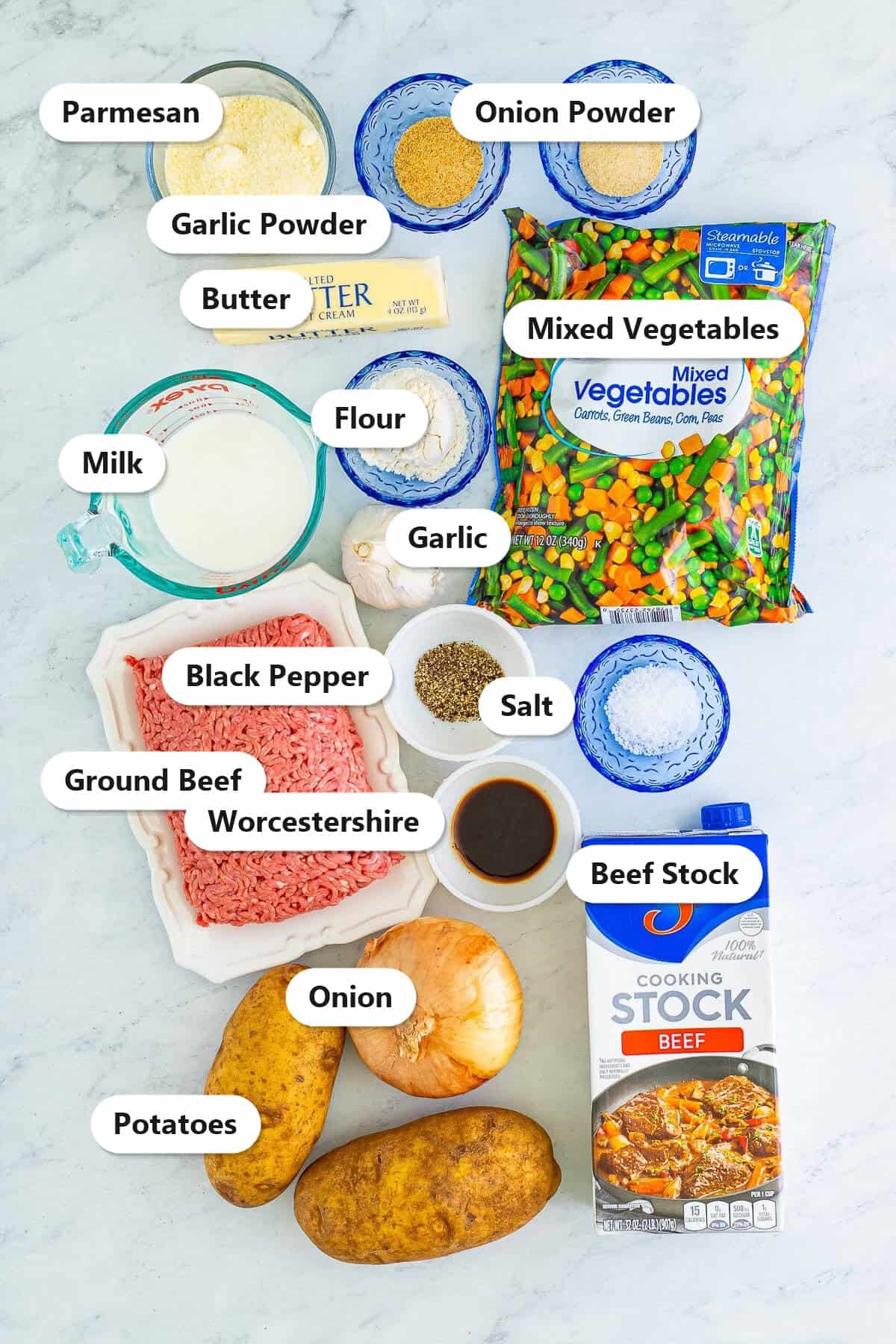 Labeled ingredients for cottage pie including ground beef, potatoes, mixed vegetables, beef stock, onion, garlic, parmesan, butter, milk, and seasonings.