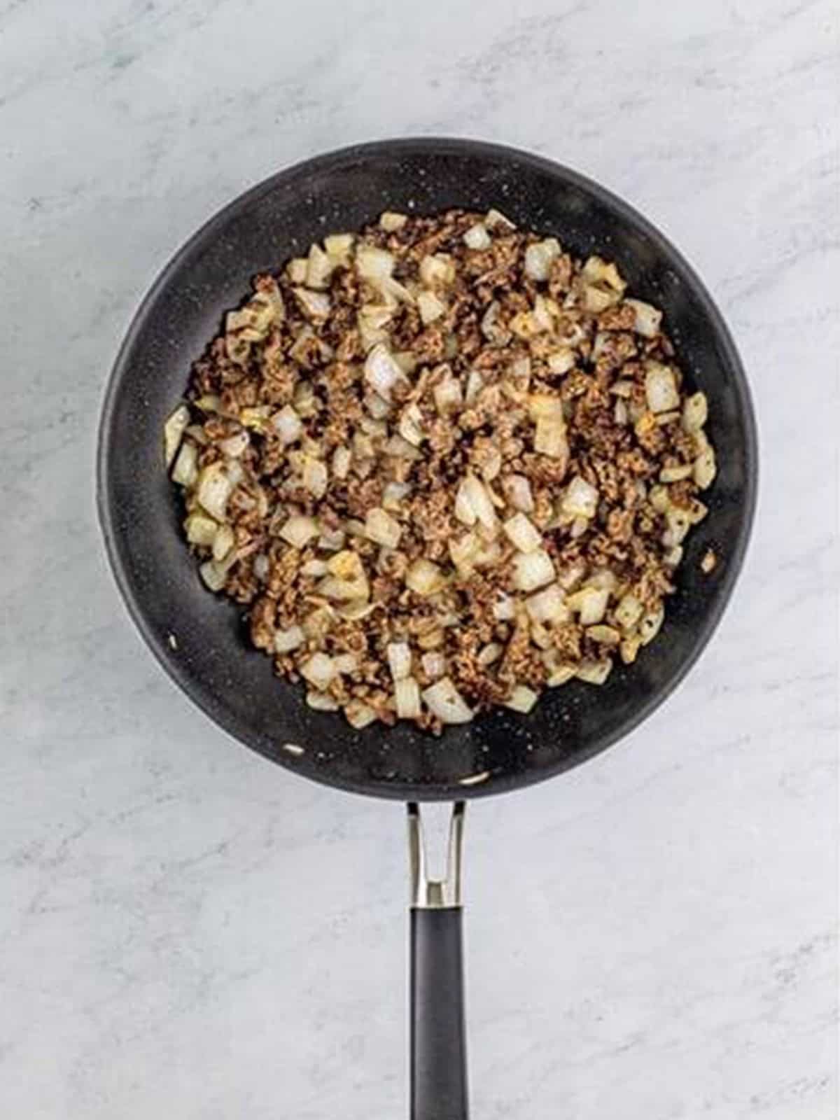 Ground beef and diced onion browning in a skillet for cottage pie filling.
