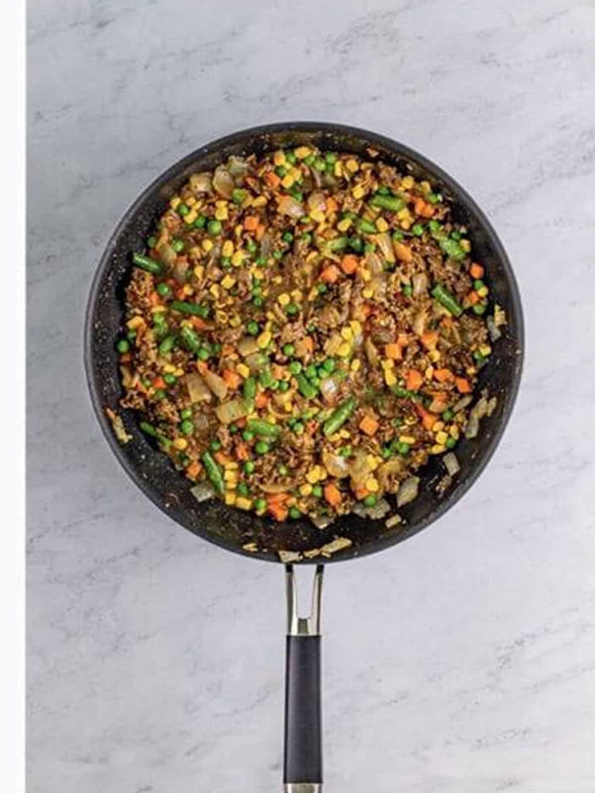 Cottage pie filling with ground beef, gravy, and mixed vegetables in a skillet.