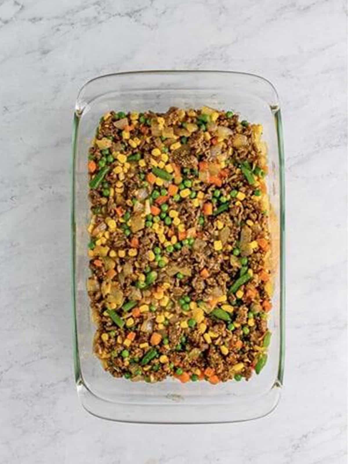 Cottage pie beef and vegetable filling layered in a glass baking dish.