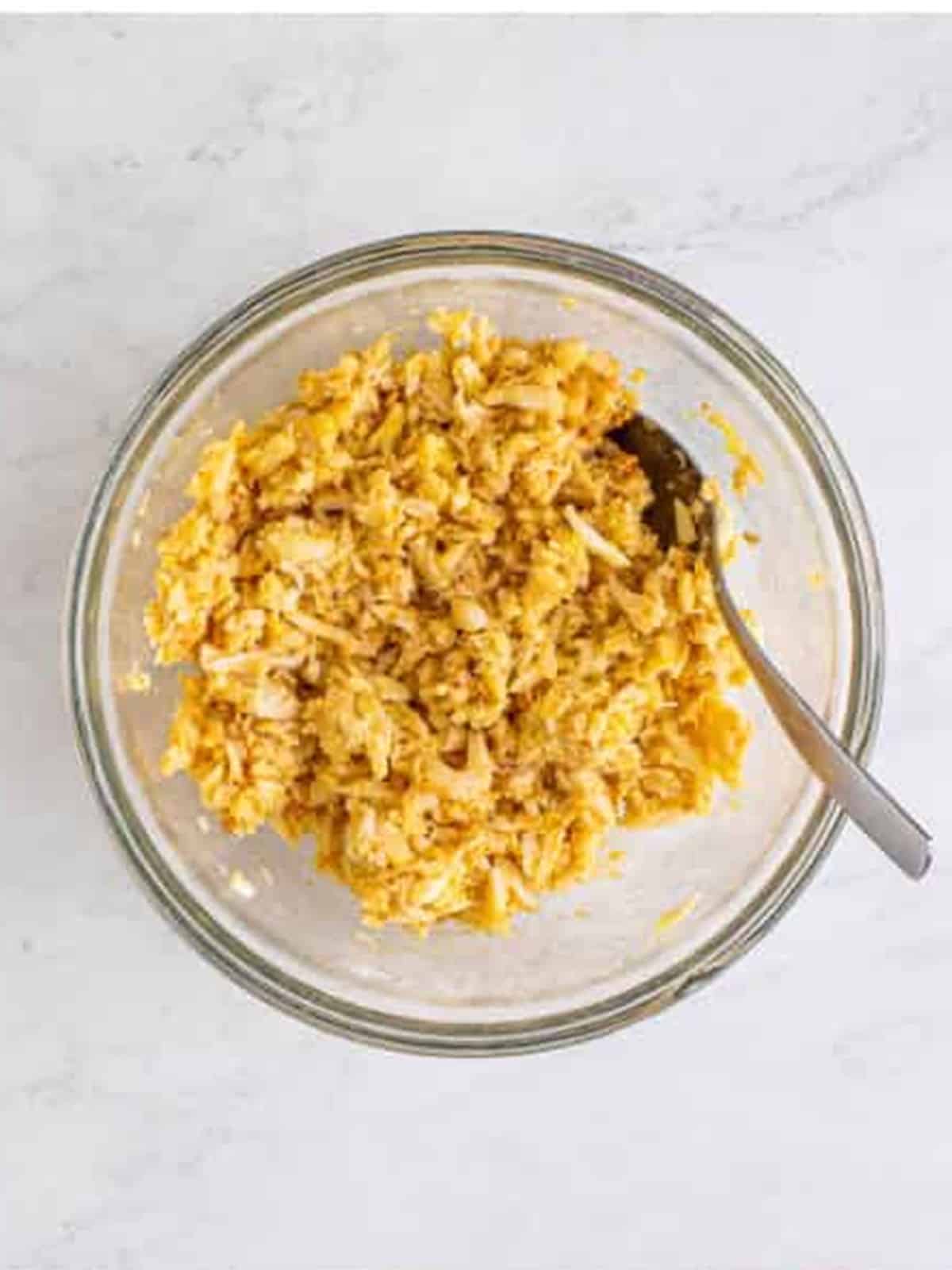 Lump crab meat mixed with egg and seasonings in a glass bowl for crab cakes.
