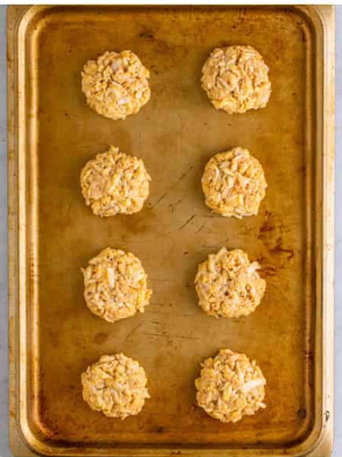 Formed crab cake patties resting on a sheet tray before frying.