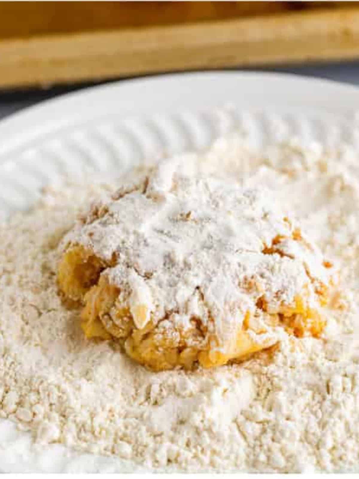A crab cake lightly dusted in flour on a plate before frying.