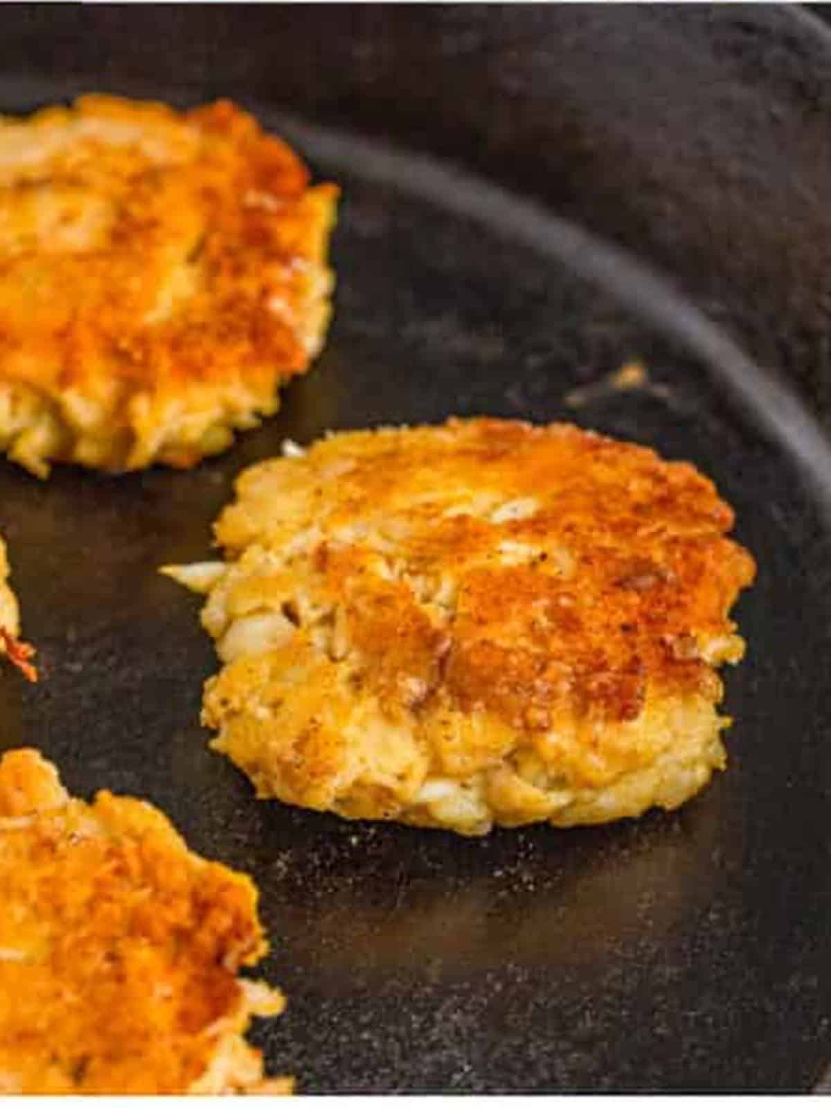 Golden brown crab cakes frying in butter in a cast iron skillet.