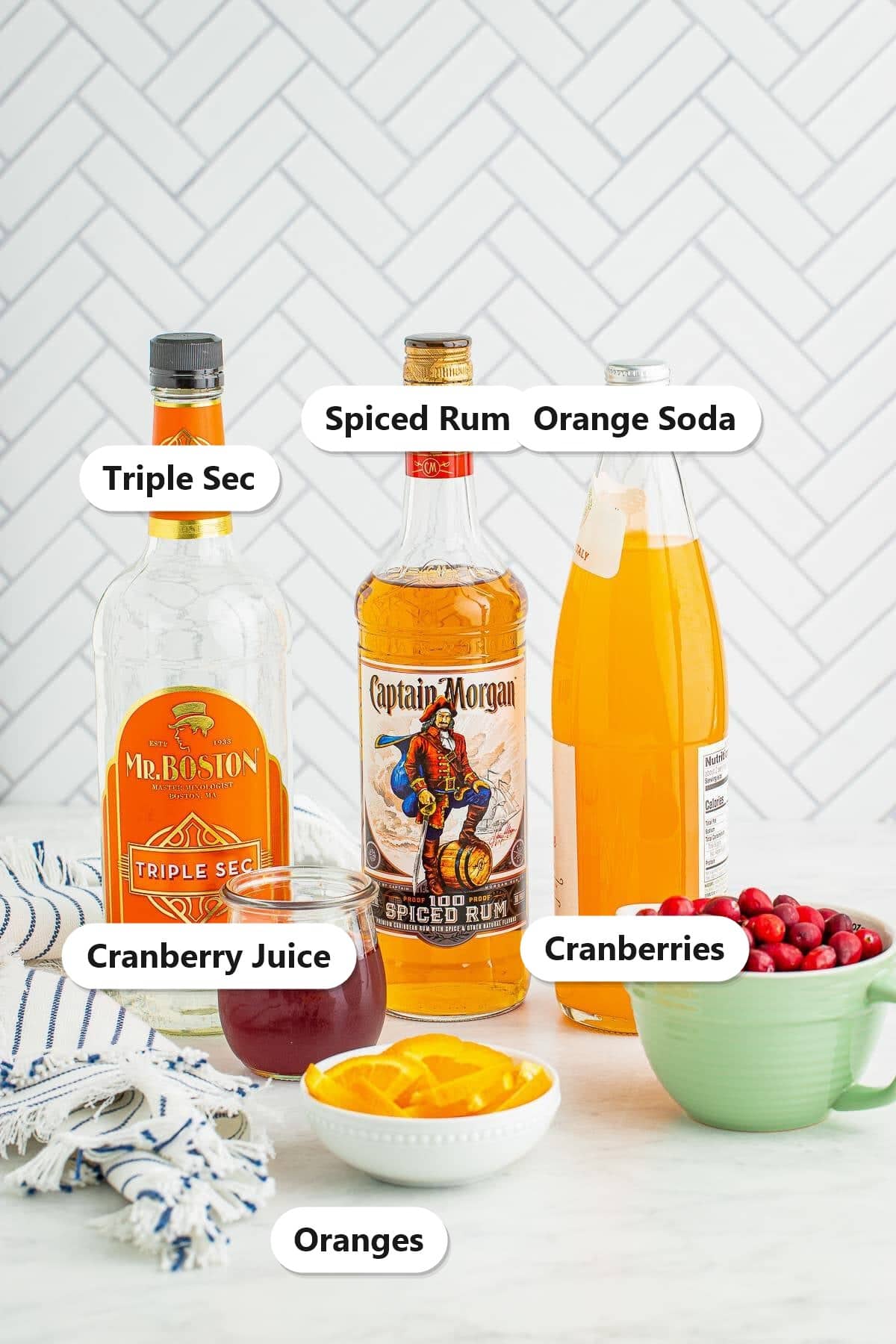 Labeled ingredients for cranberry orange rum punch including spiced rum, triple sec, orange soda, cranberry juice, cranberries, and oranges.
