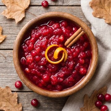 An overhead wooden bowl of homemade cranberry sauce with a cinnamon stick and orange peel, fall styling.