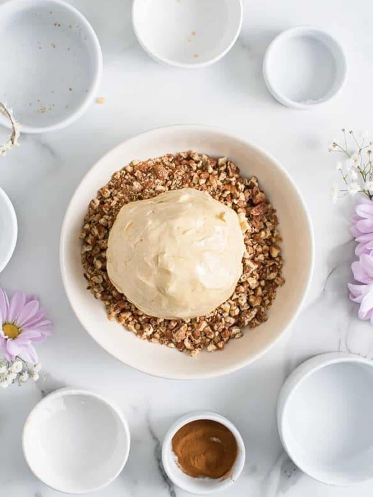 A cream cheese ball being rolled in crushed praline pecans in a shallow dish.