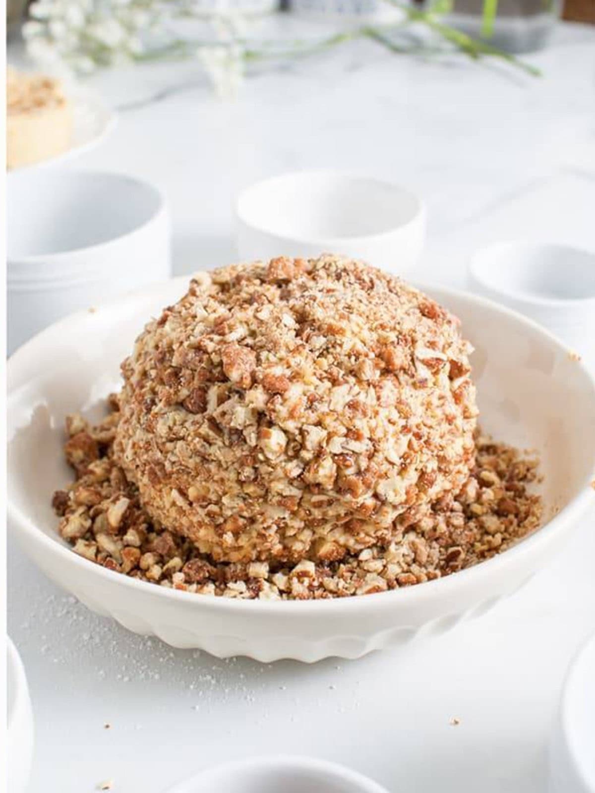 A finished cinnamon cream cheese ball coated in praline pecans on a white serving plate.