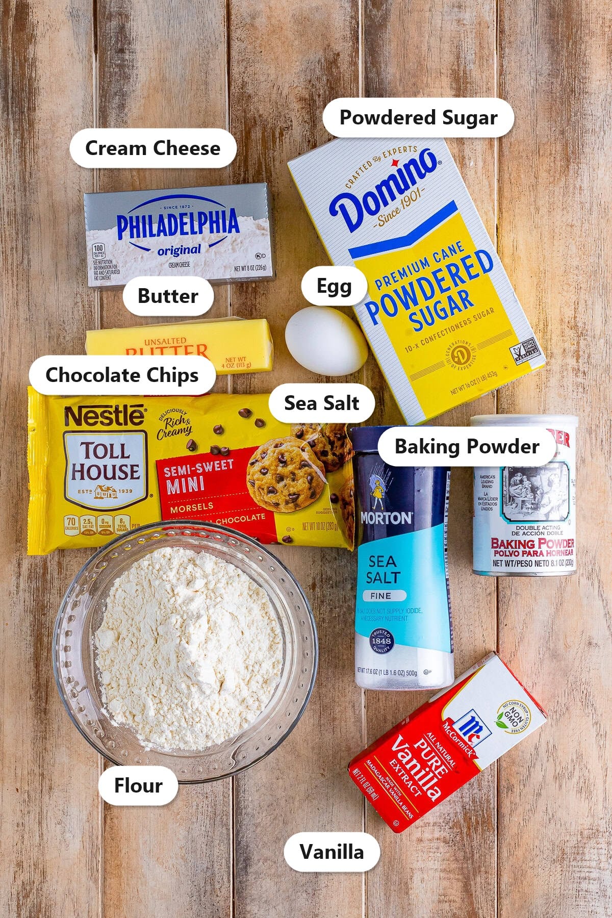 Labeled ingredients for cream cheese chocolate chip cookies including cream cheese, butter, powdered sugar, egg, flour, mini chocolate chips, baking powder, sea salt, and vanilla.