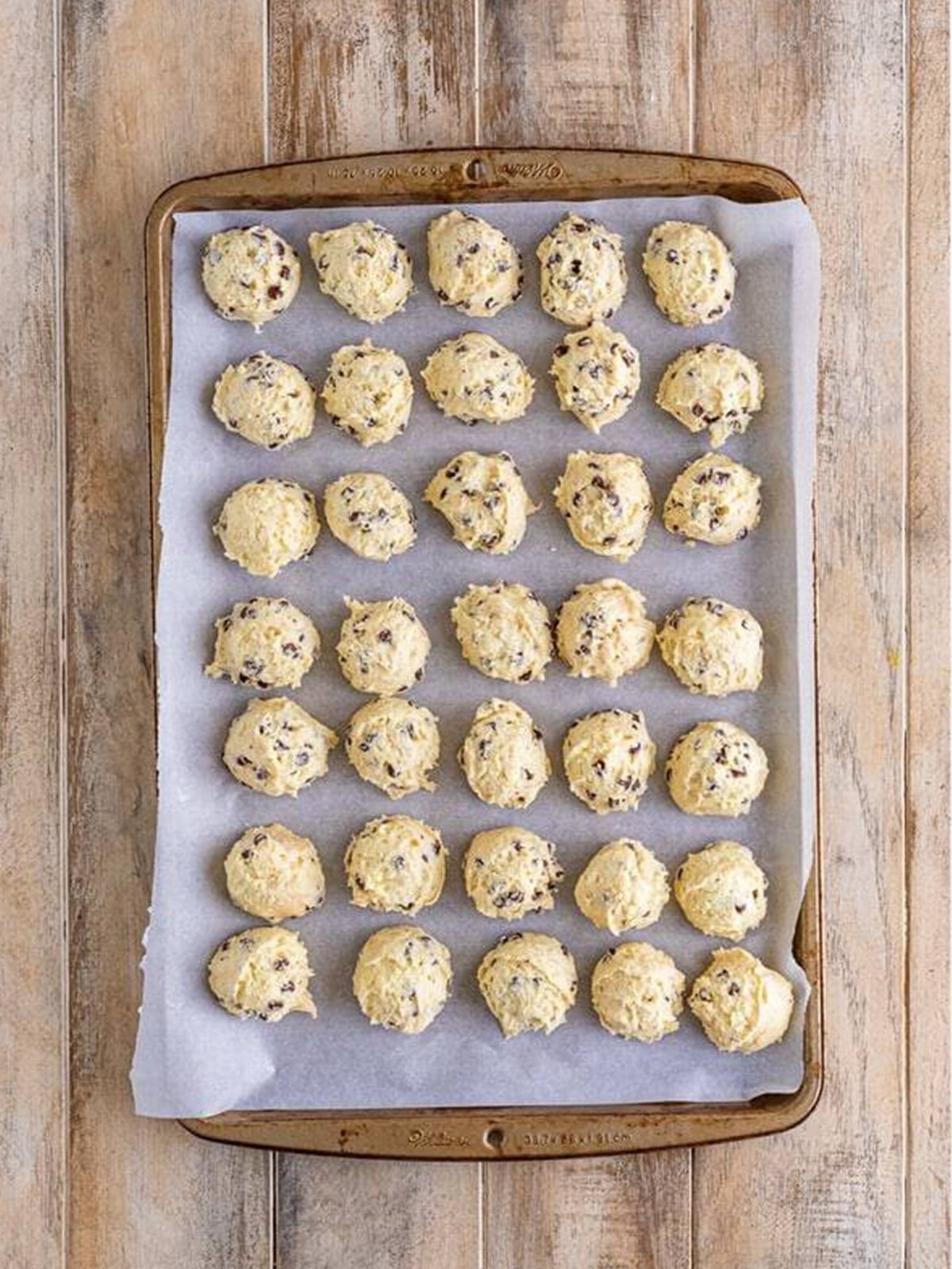 Scooped cream cheese cookie dough balls on a parchment lined baking sheet.