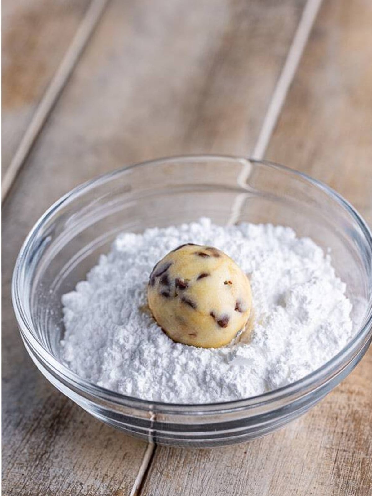 Rolling a cream cheese cookie dough ball in powdered sugar.
