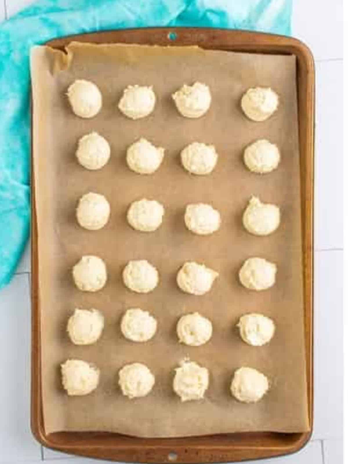 Scooped dollops of cream cheese cookie dough on a parchment lined tray ready to chill.