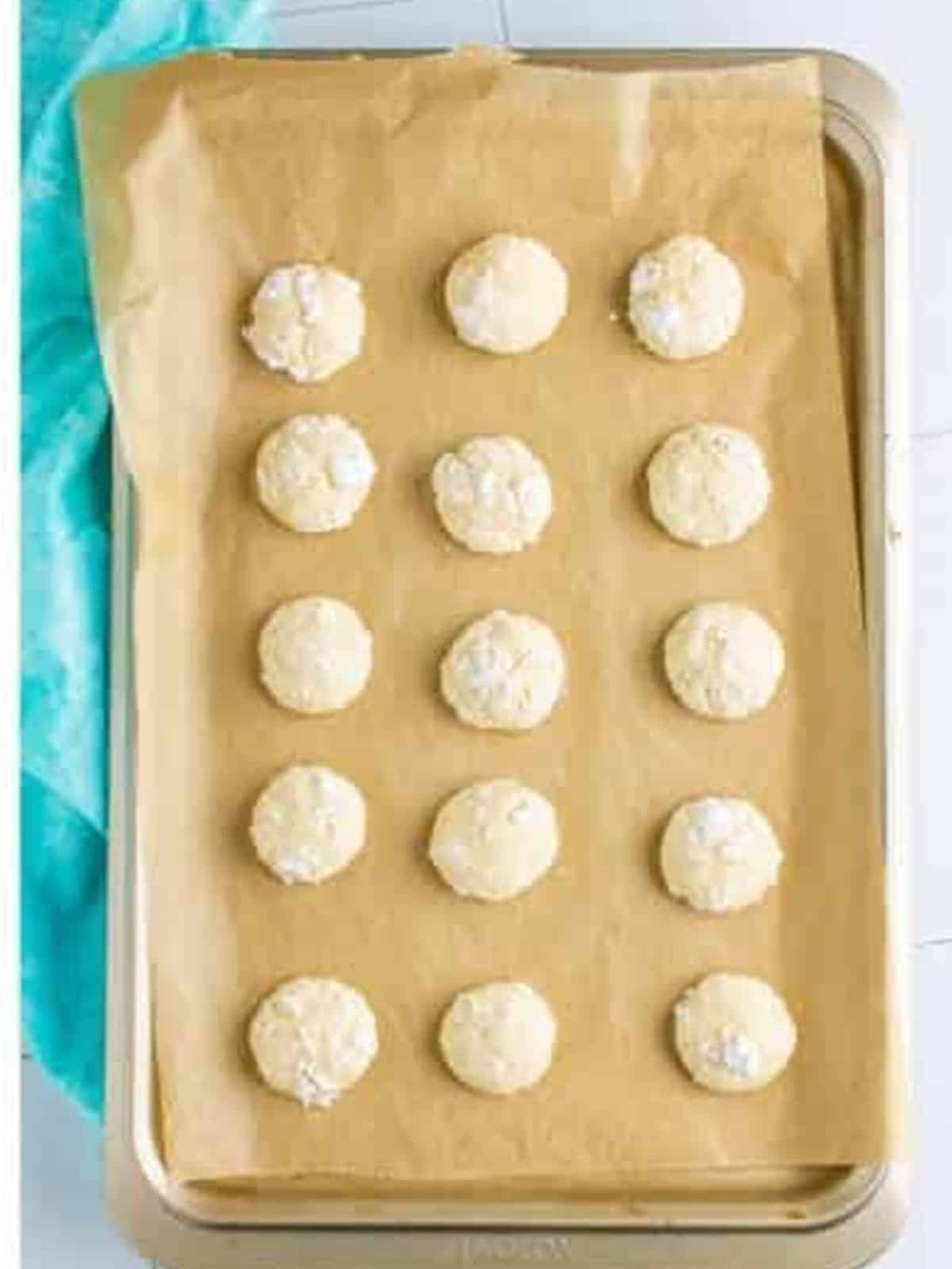Baked cream cheese cookies with crackly powdered sugar tops on a baking sheet.