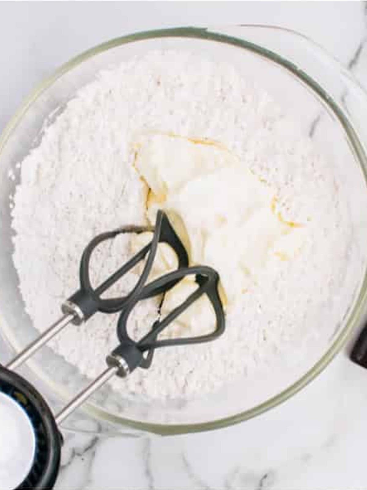Cream cheese and powdered sugar combined in a glass bowl with beaters.