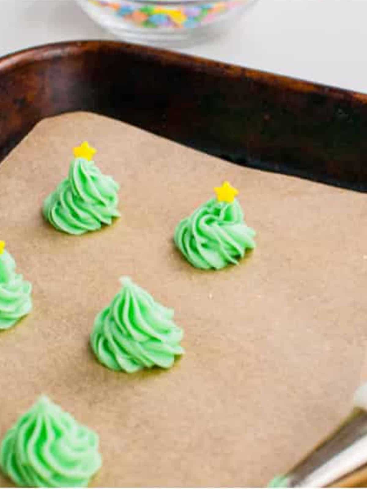 Green cream cheese mints piped into shapes on a parchment-lined tray.