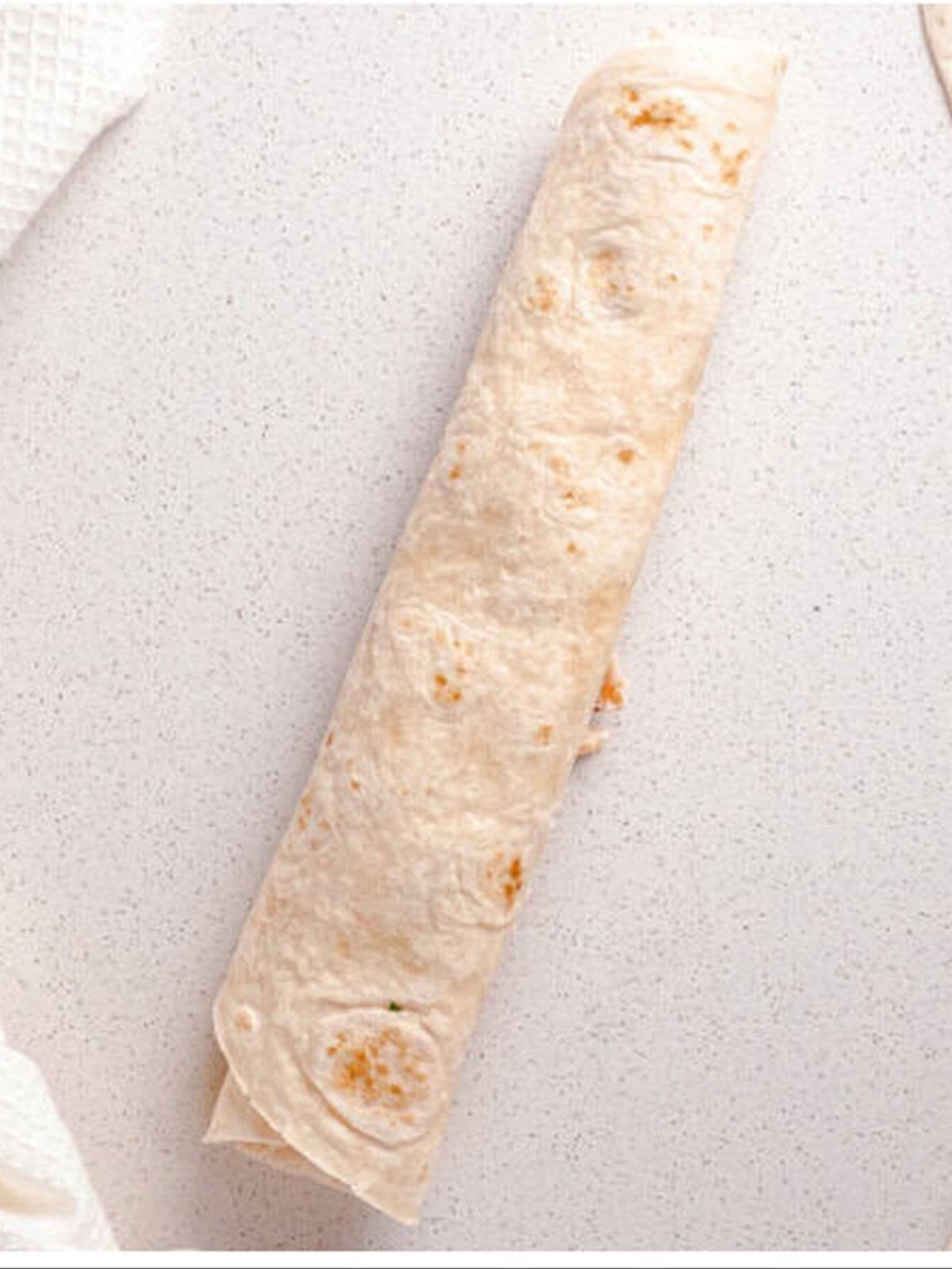 A filled tortilla rolled tightly into a log to make pinwheels.