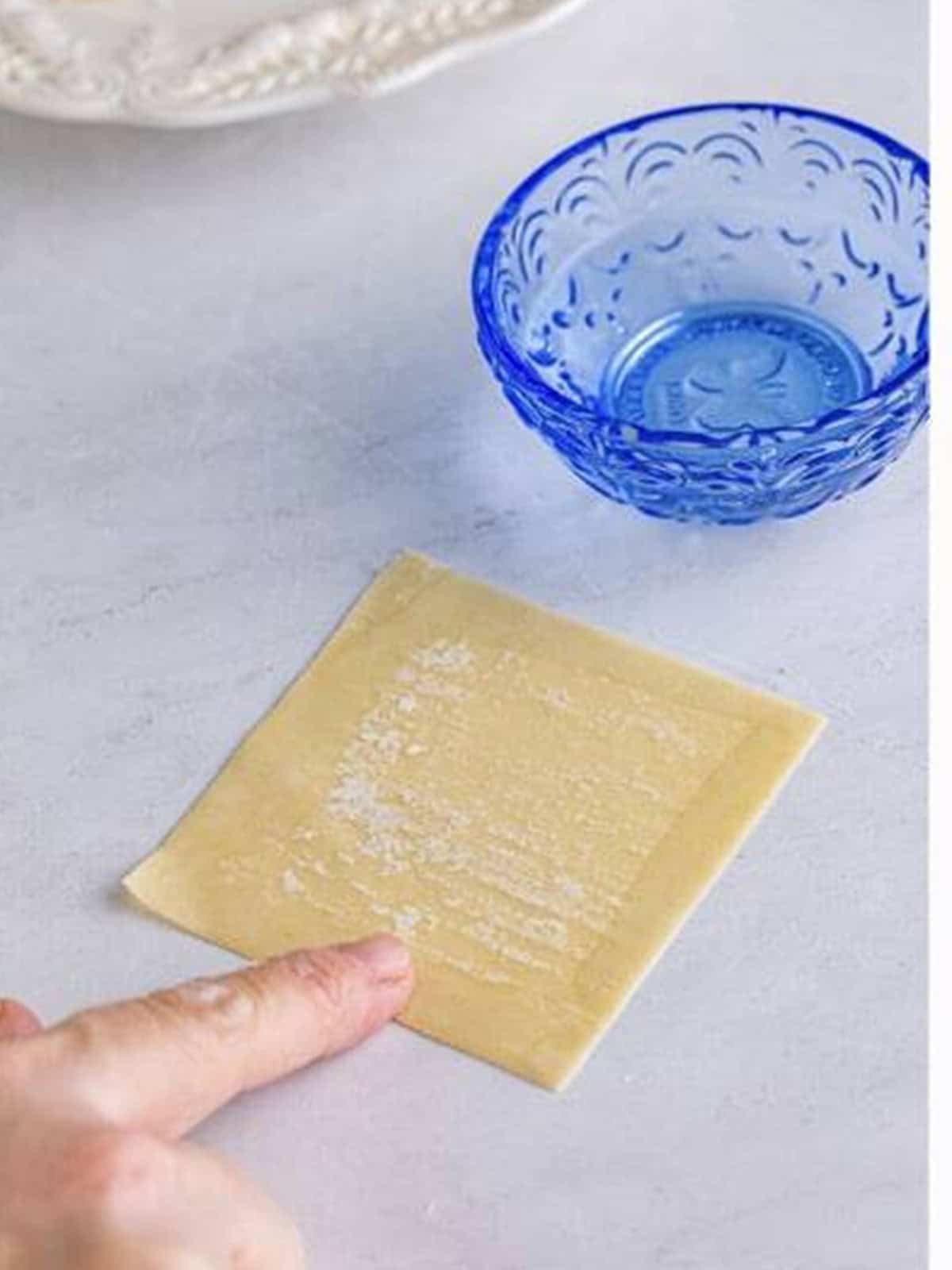 A wonton wrapper with its edges moistened with water on a work surface.