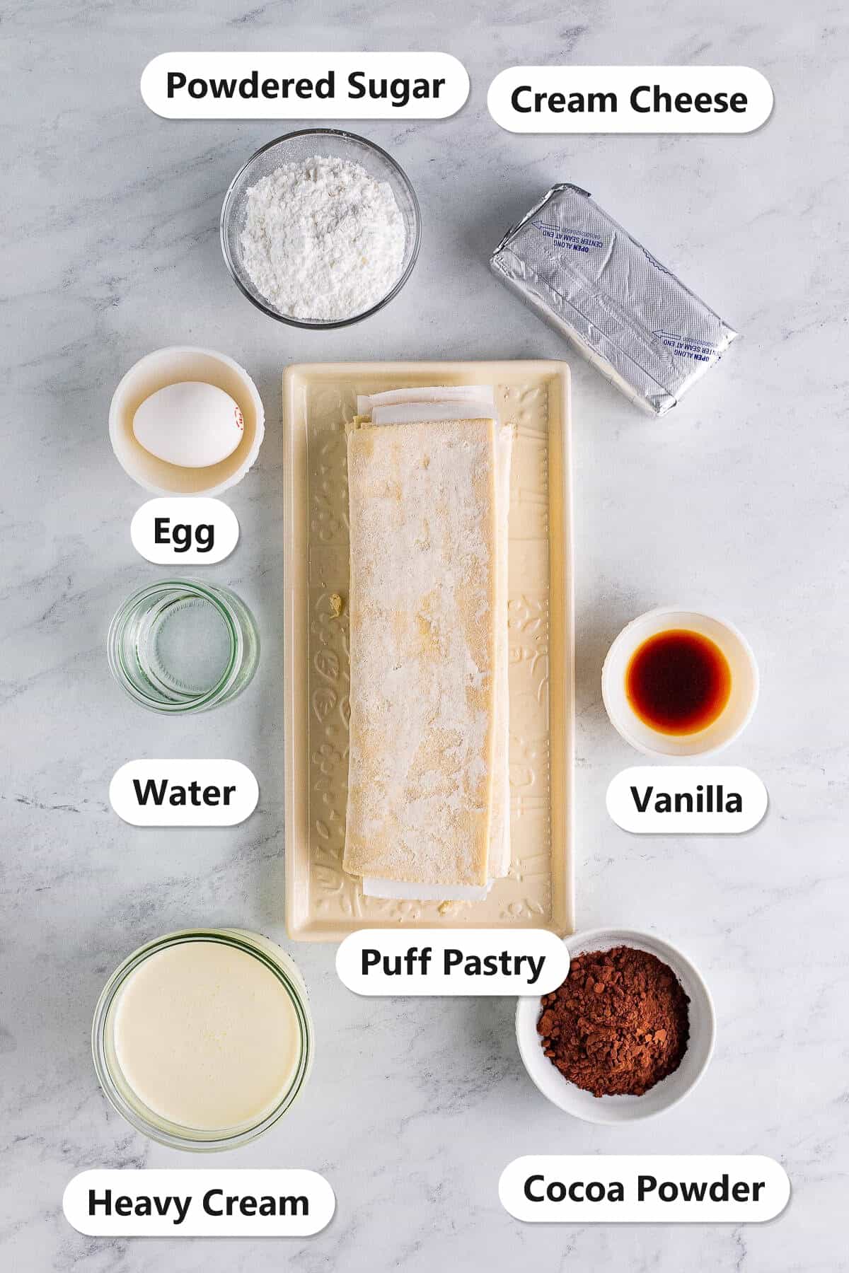Labeled ingredients for cream horns including puff pastry, cream cheese, powdered sugar, heavy cream, egg, vanilla, water, and cocoa powder.