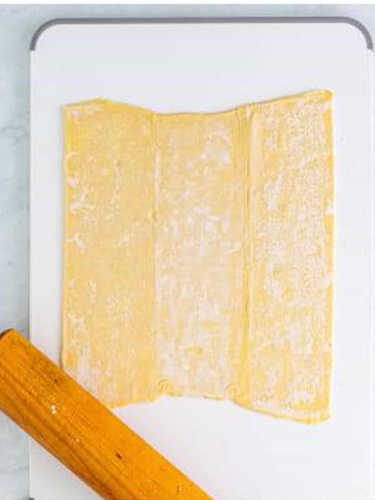 Flattening a sheet of puff pastry with a rolling pin for cream horns.