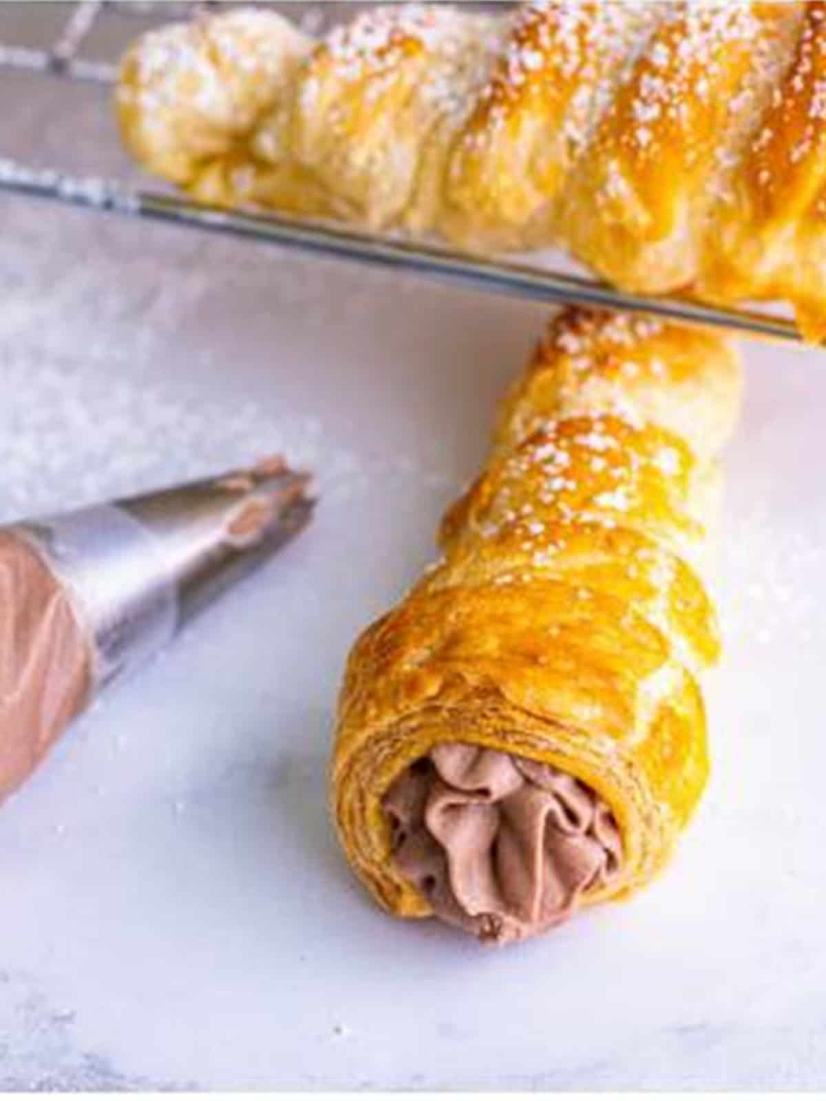 Piping vanilla cream filling into a baked cream horn with a star tip.