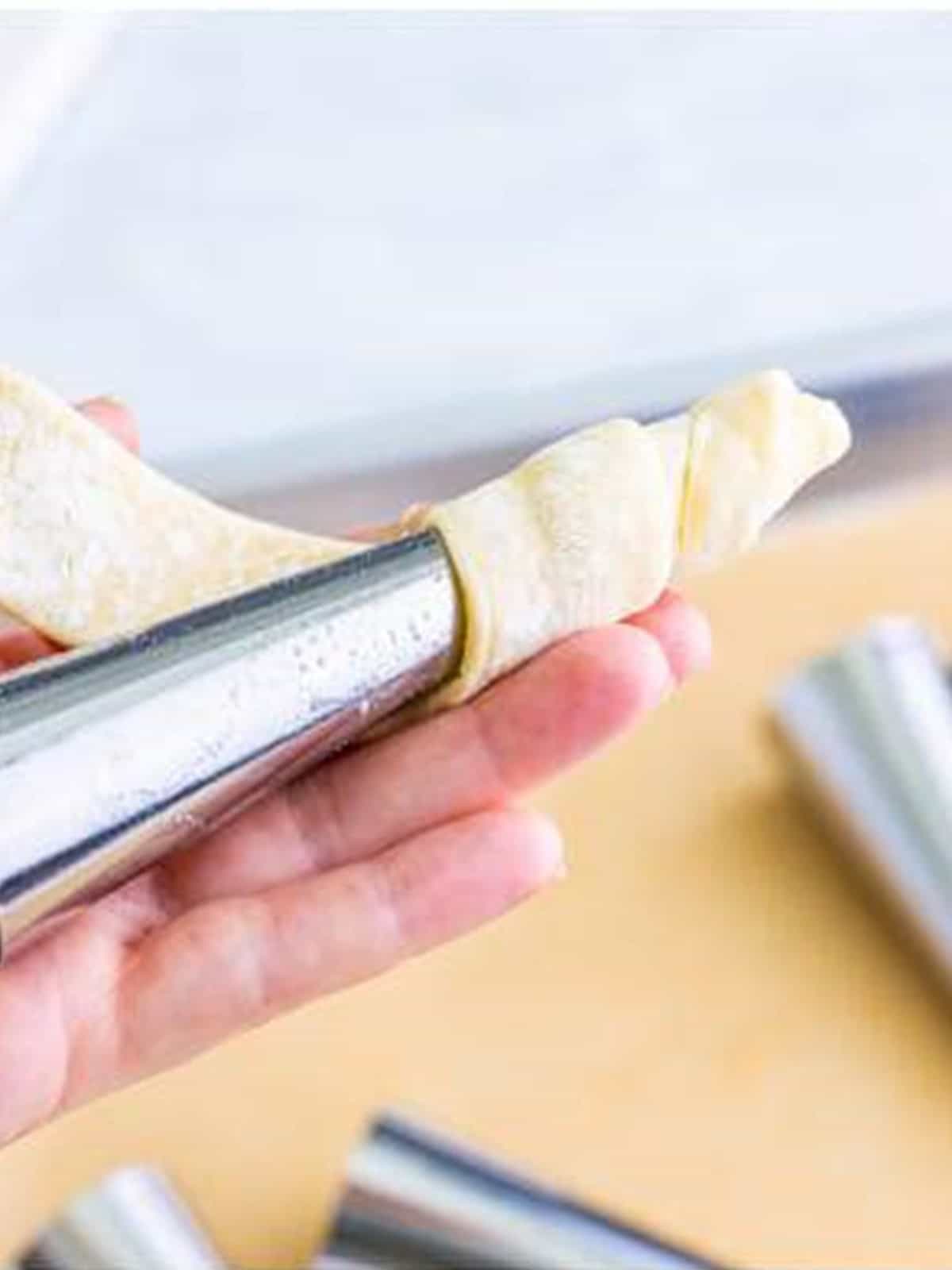 Wrapping a puff pastry strip around a cream horn mold.