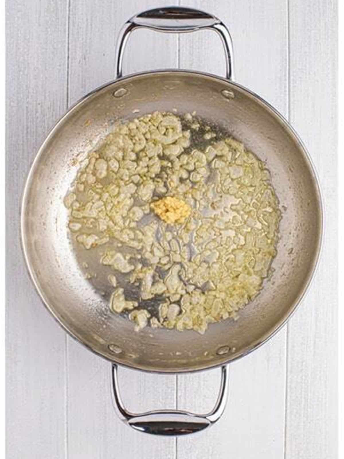 Minced garlic added to the sauteed onions in a skillet.