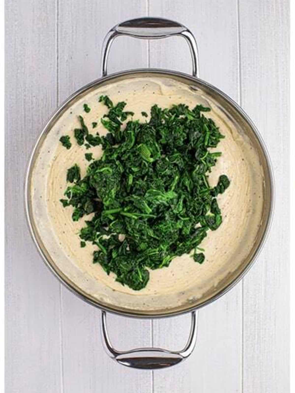 Thawed spinach stirred into the creamy sauce in a skillet.