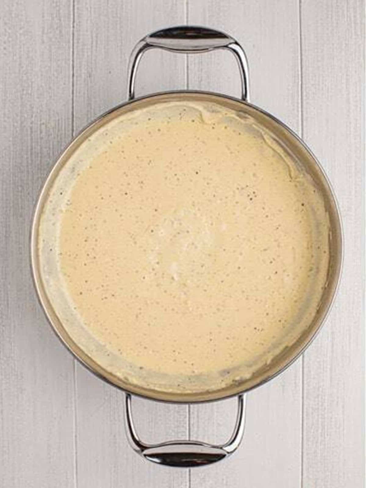 A smooth creamy parmesan sauce cooked in a skillet for creamed spinach.