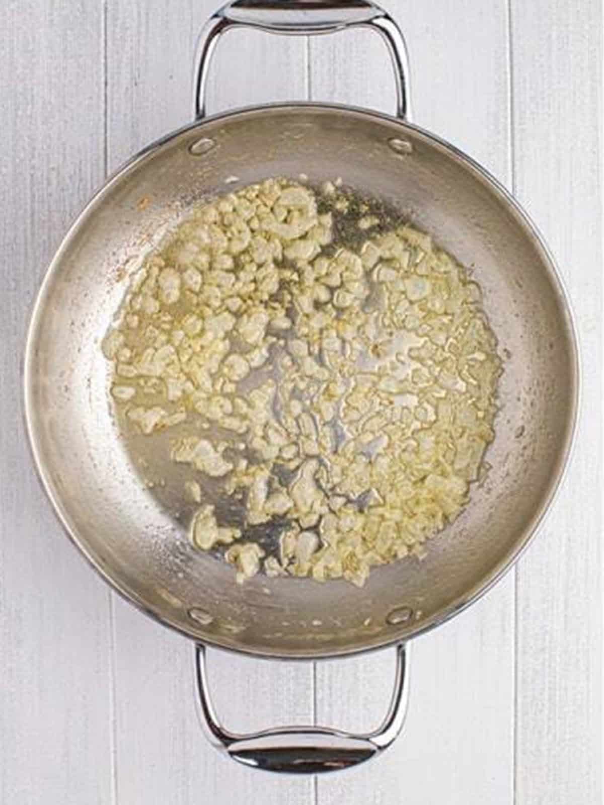 Diced onion sauteing in melted butter in a stainless steel skillet.