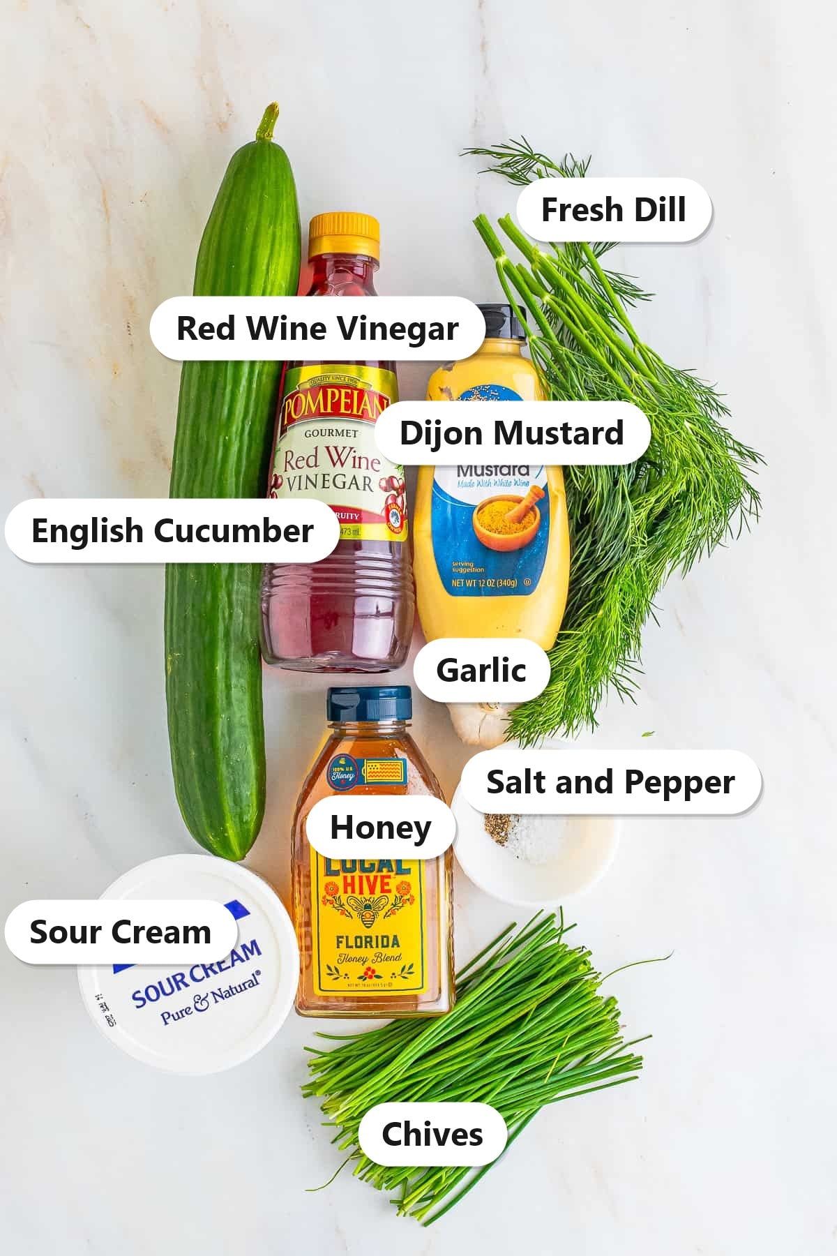 Labeled ingredients for creamy cucumber salad including English cucumber, sour cream, red wine vinegar, Dijon mustard, honey, garlic, fresh dill, chives, and salt and pepper.