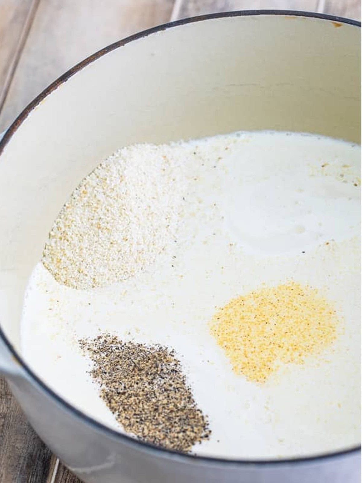 Grits, cream, chicken stock, and seasonings added to a pot to make creamy grits.