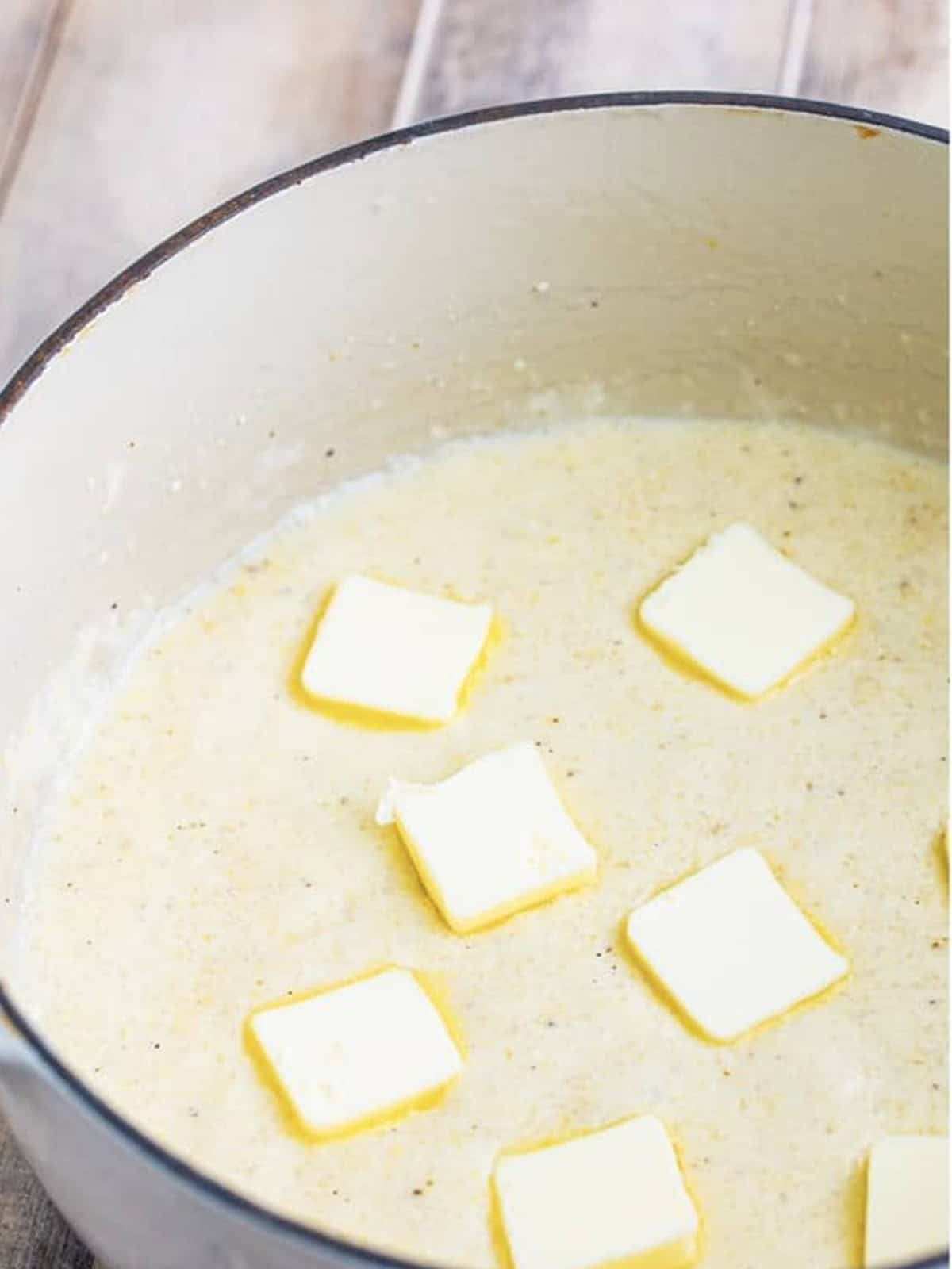 Pats of butter added to the cooked creamy grits in a pot.