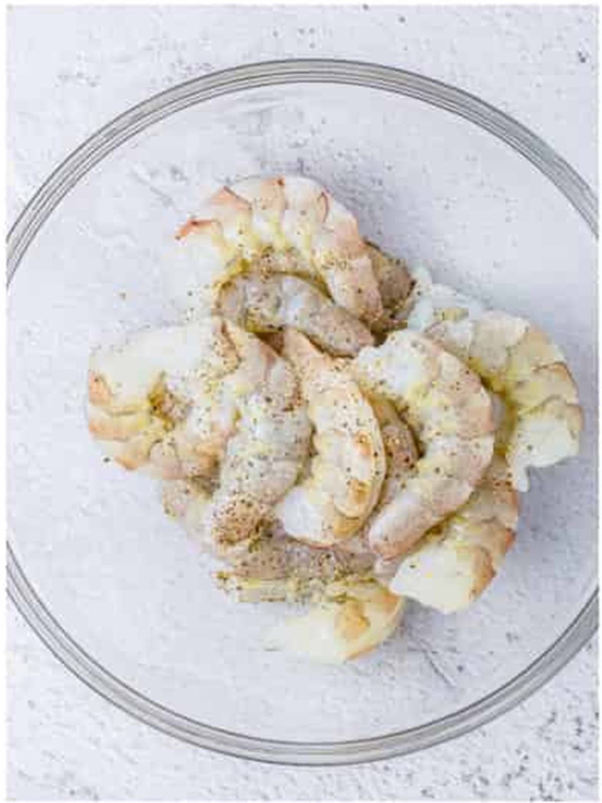 Raw shrimp tossed with salt and pepper in a glass bowl for creamy lemon shrimp.