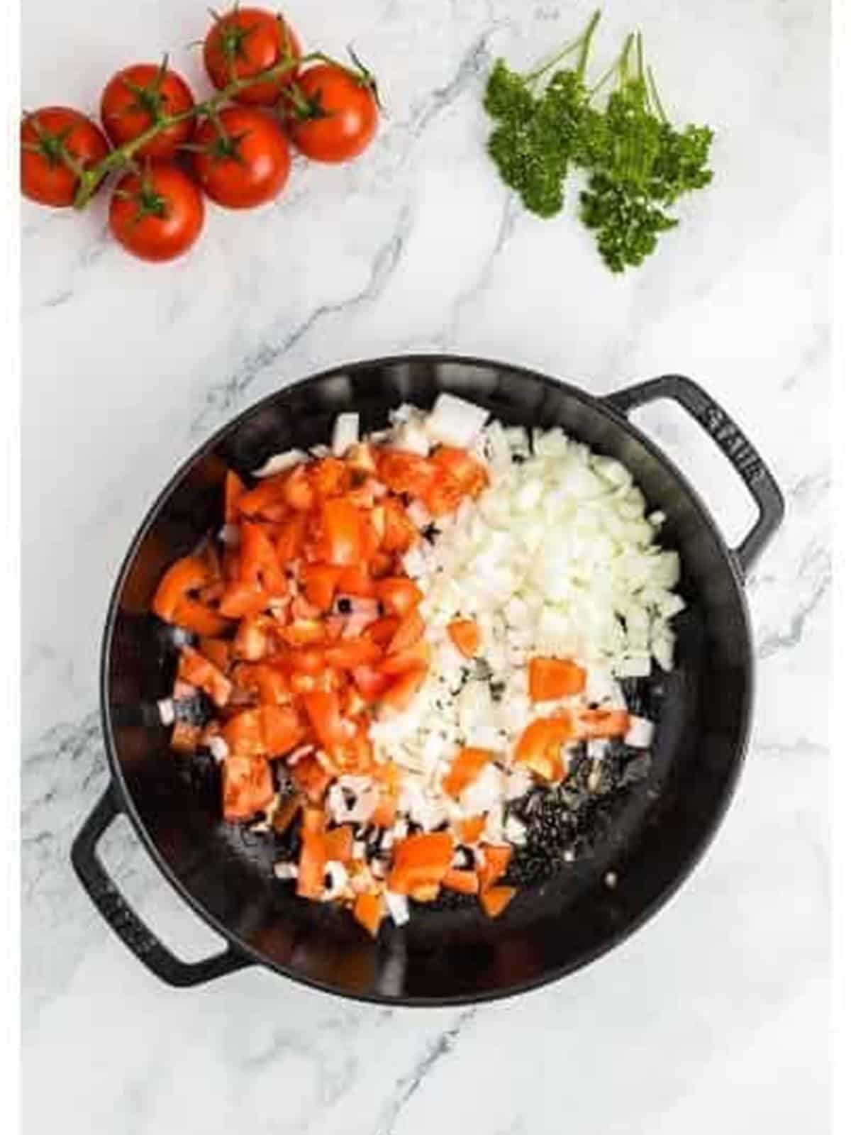 Diced onion and tomatoes cooking in the skillet for paprika chicken.
