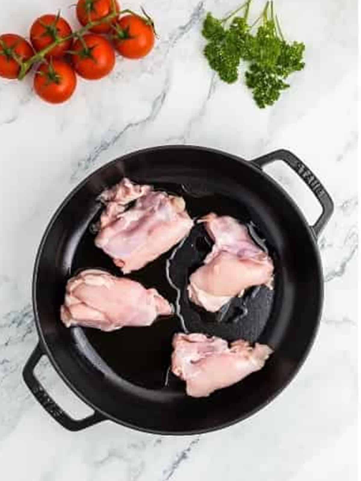 Boneless chicken thighs searing in a black skillet for creamy paprika chicken.