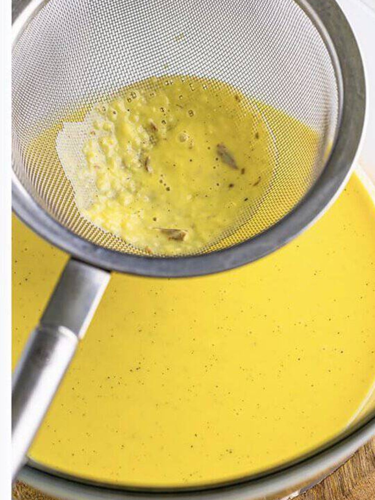 Straining the finished creme anglaise through a fine mesh strainer.