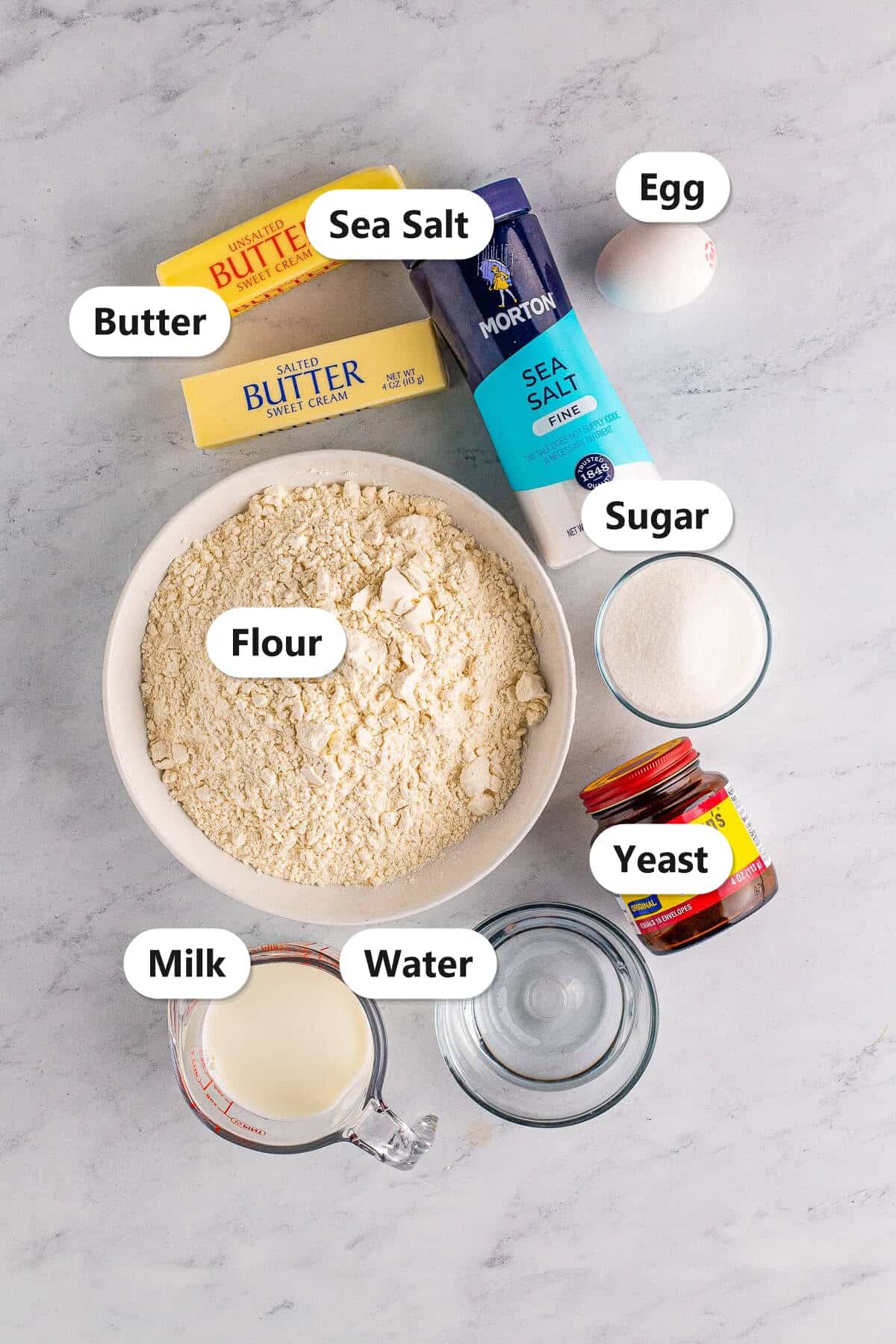 Labeled ingredients for homemade crescent rolls including butter, sea salt, egg, flour, sugar, yeast, milk, and water.