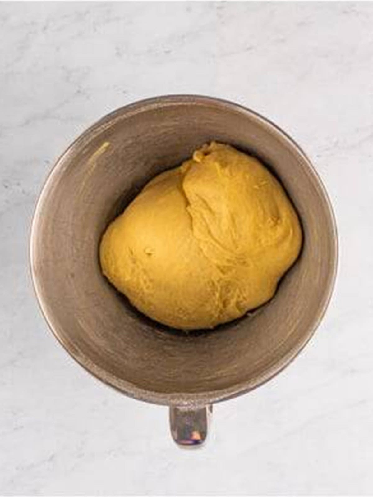 Soft crescent roll dough mixed into a ball in a stand mixer bowl.