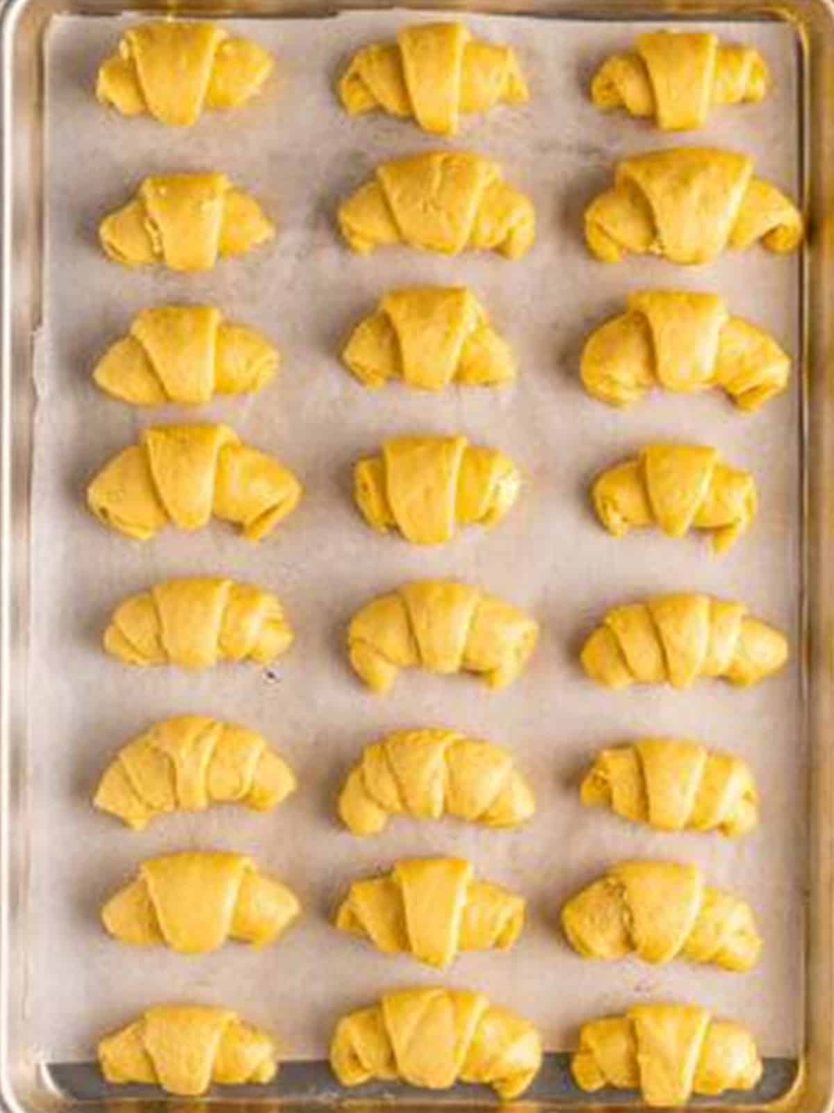Shaped raw crescent rolls arranged on a parchment lined baking sheet.