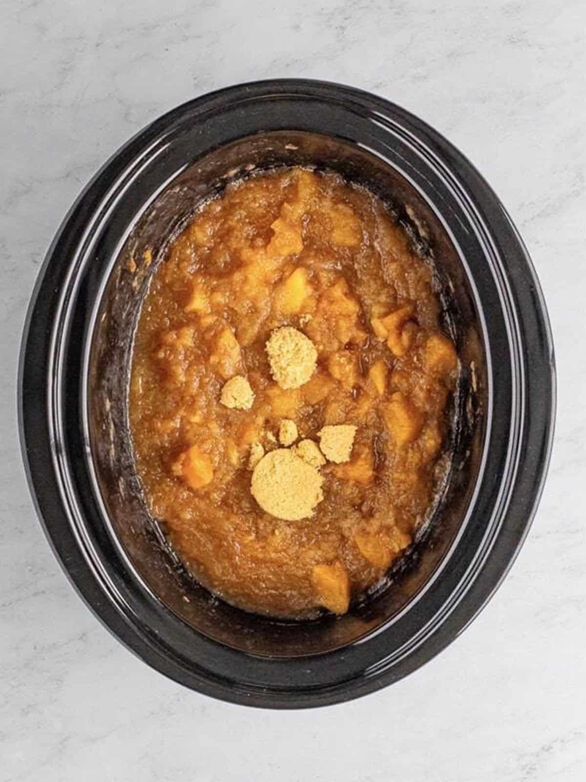 Cooked apples mashed into chunky crock pot applesauce with a wooden spoon.